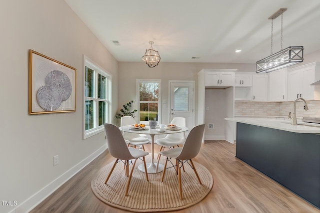 dining area featuring a chandelier, baseboards, visible vents, and light wood finished floors