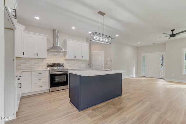 kitchen featuring light countertops, electric range, backsplash, a sink, and wall chimney range hood