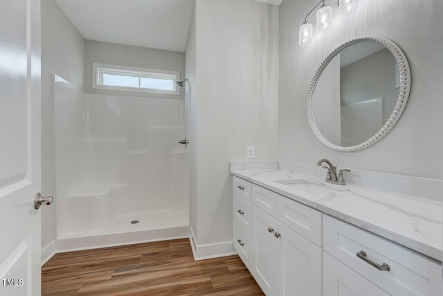 bathroom with baseboards, walk in shower, wood finished floors, and vanity