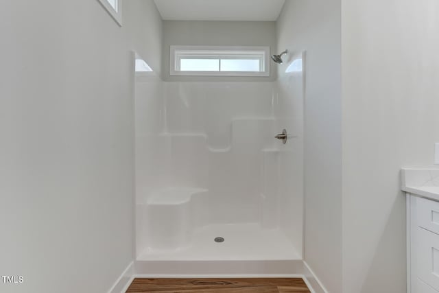 full bath featuring wood finished floors, vanity, baseboards, and walk in shower