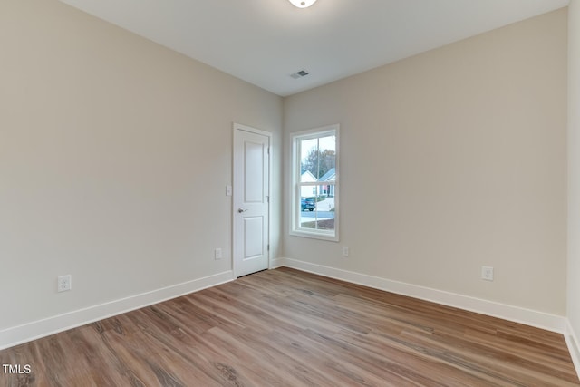 spare room with light wood finished floors, visible vents, and baseboards