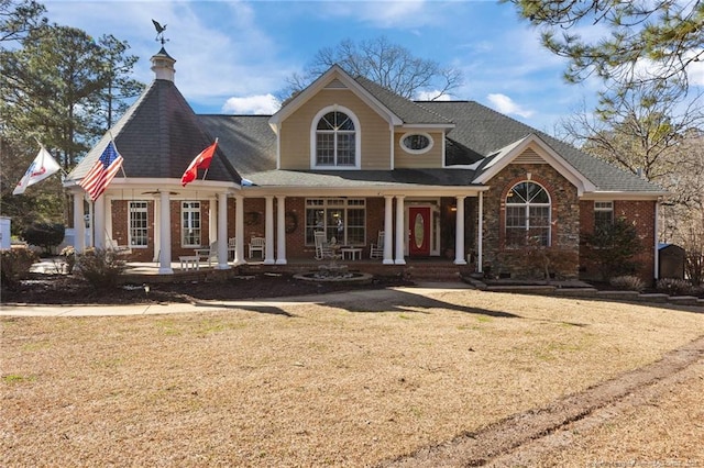 view of front facade with a porch, a front yard, and brick siding