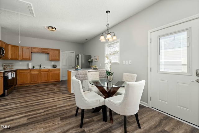 dining space with attic access, dark wood finished floors, a textured ceiling, and an inviting chandelier