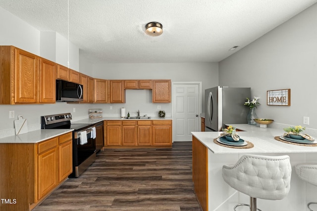 kitchen featuring stainless steel appliances, dark wood-type flooring, a sink, a peninsula, and a kitchen breakfast bar