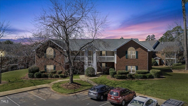 view of front of property with a balcony, a yard, uncovered parking, and brick siding