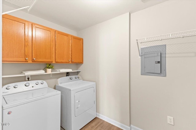 laundry room with washing machine and dryer, light wood-style floors, baseboards, cabinet space, and electric panel