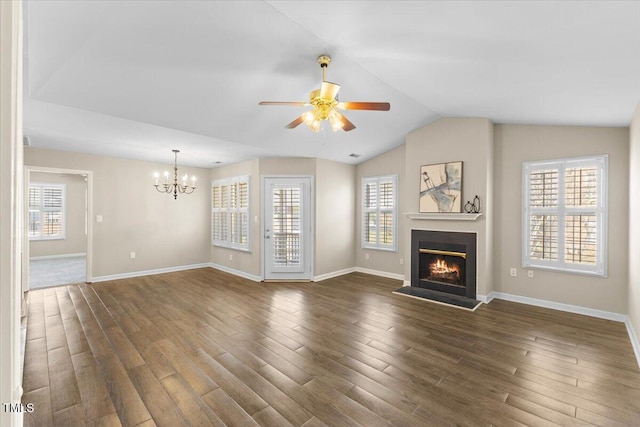 unfurnished living room with a healthy amount of sunlight, a lit fireplace, vaulted ceiling, and dark wood finished floors