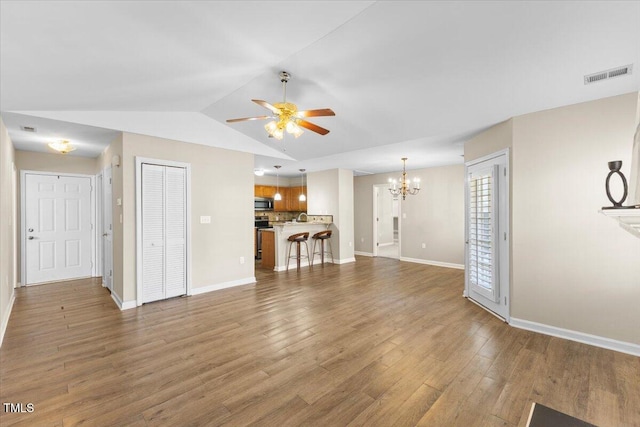 unfurnished living room featuring visible vents, vaulted ceiling, wood finished floors, baseboards, and ceiling fan with notable chandelier