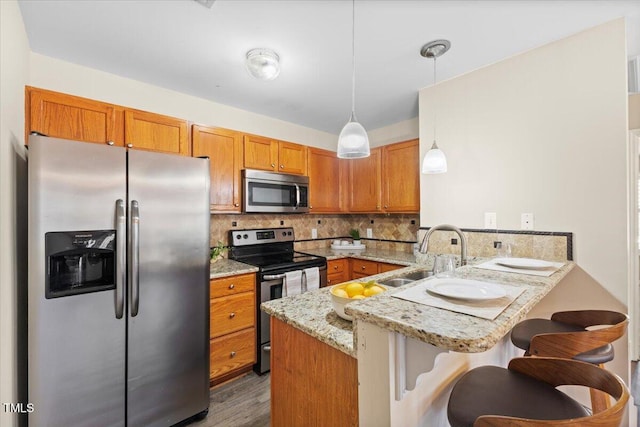 kitchen featuring decorative backsplash, brown cabinets, a peninsula, stainless steel appliances, and a sink