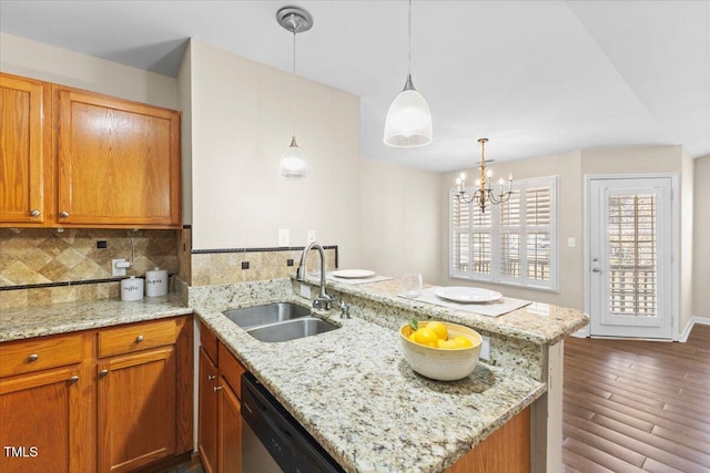 kitchen with a peninsula, a sink, backsplash, light stone countertops, and dark wood finished floors