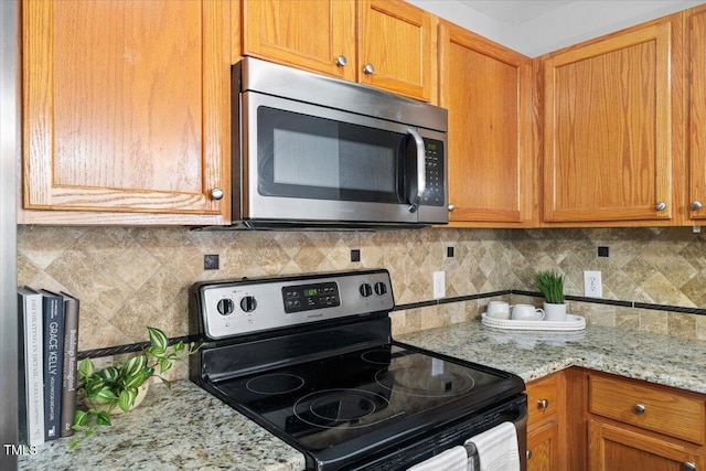 kitchen featuring brown cabinetry, tasteful backsplash, light stone counters, and stainless steel appliances