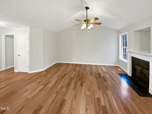 unfurnished living room featuring lofted ceiling, wood finished floors, a fireplace with flush hearth, and baseboards