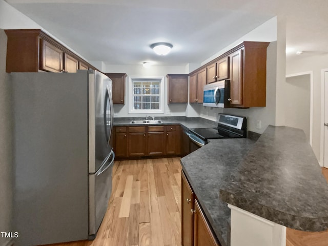 kitchen with a peninsula, light wood finished floors, stainless steel appliances, and a sink