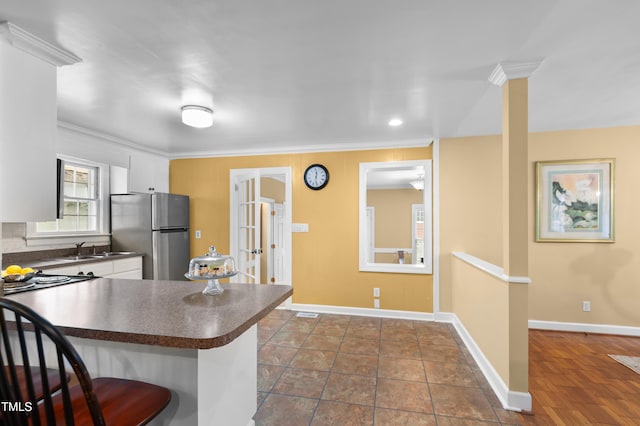 kitchen featuring dark countertops, freestanding refrigerator, white cabinetry, a sink, and a kitchen bar