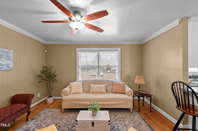 living room featuring ceiling fan, crown molding, baseboards, and wood finished floors