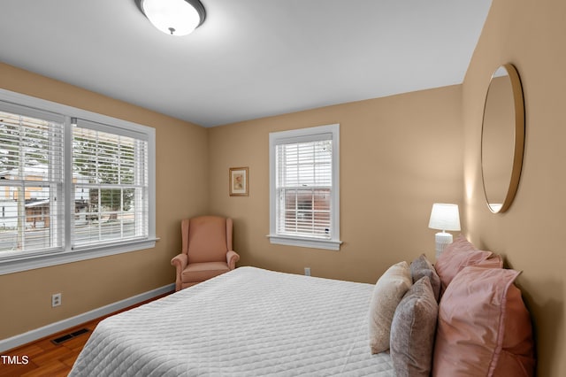 bedroom with baseboards, visible vents, and wood finished floors