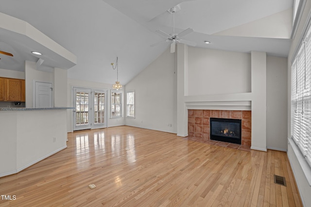 unfurnished living room featuring visible vents, high vaulted ceiling, a ceiling fan, a fireplace, and light wood finished floors