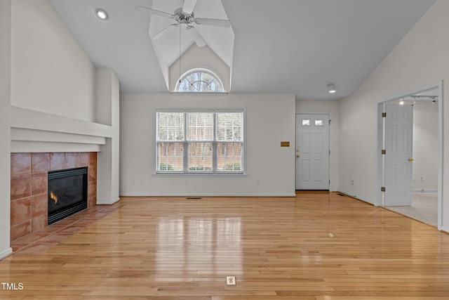 unfurnished living room with baseboards, a tiled fireplace, lofted ceiling, light wood-style floors, and a ceiling fan