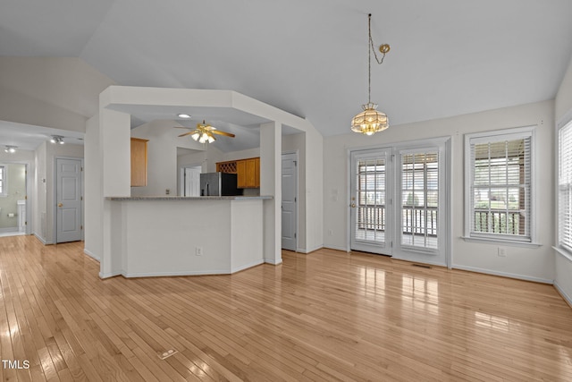 unfurnished living room featuring lofted ceiling, ceiling fan with notable chandelier, light wood-type flooring, and baseboards