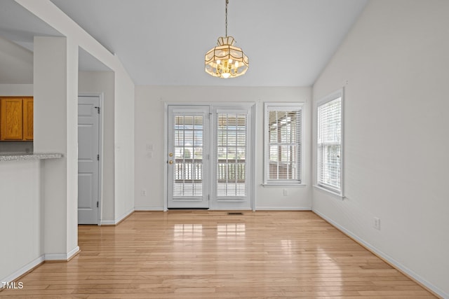 unfurnished dining area featuring light wood-style flooring, baseboards, a chandelier, and vaulted ceiling