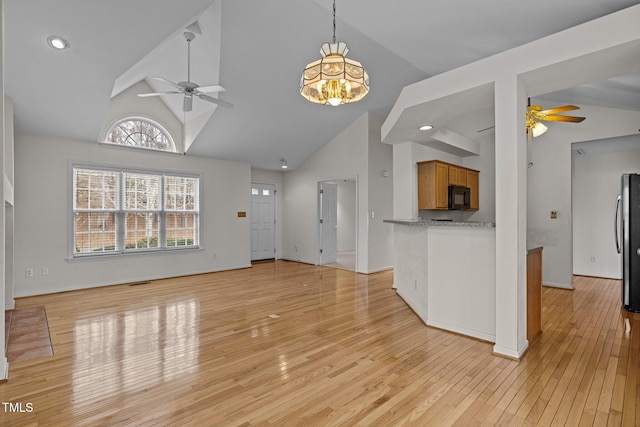 unfurnished living room featuring ceiling fan with notable chandelier, high vaulted ceiling, light wood-type flooring, and baseboards