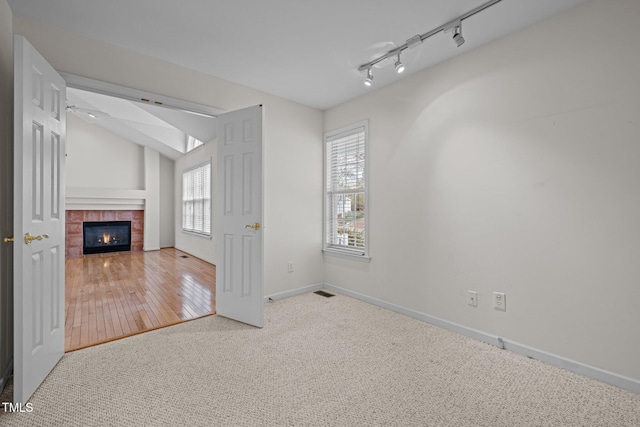 unfurnished living room featuring lofted ceiling, track lighting, a tiled fireplace, carpet, and baseboards