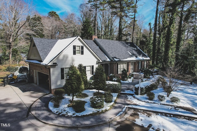 view of front facade with brick siding, roof with shingles, a chimney, concrete driveway, and a garage