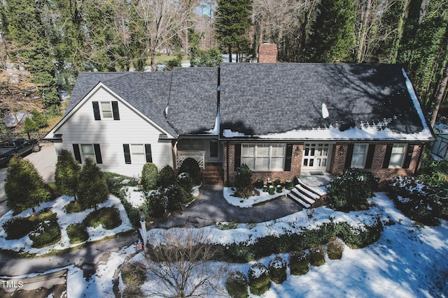 view of front facade featuring a shingled roof, brick siding, and a chimney