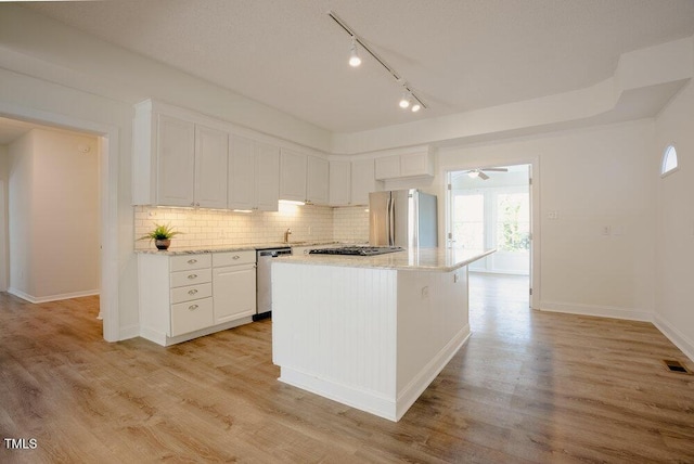 kitchen featuring light wood finished floors, tasteful backsplash, a center island, stainless steel appliances, and white cabinetry