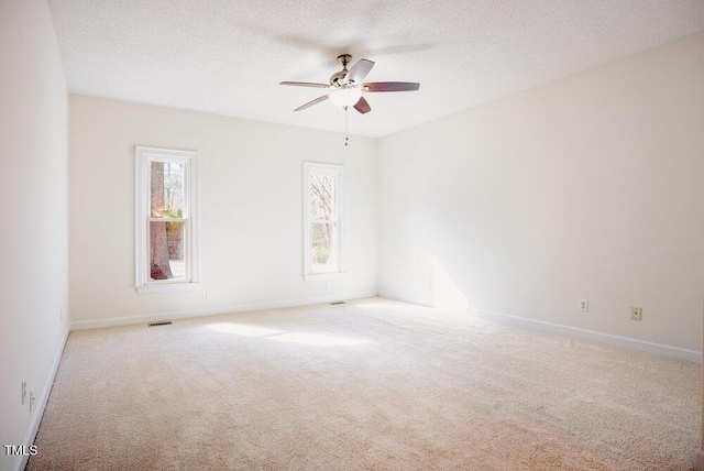 carpeted empty room featuring a ceiling fan, visible vents, a textured ceiling, and baseboards