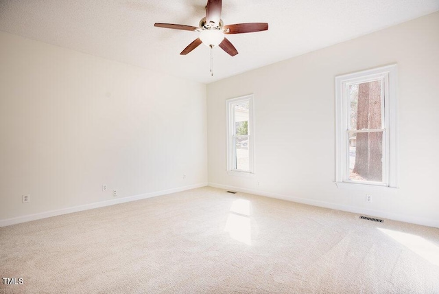 carpeted empty room featuring a ceiling fan, visible vents, a textured ceiling, and baseboards