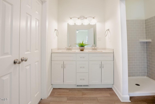 bathroom featuring double vanity, tiled shower, a sink, and wood finished floors