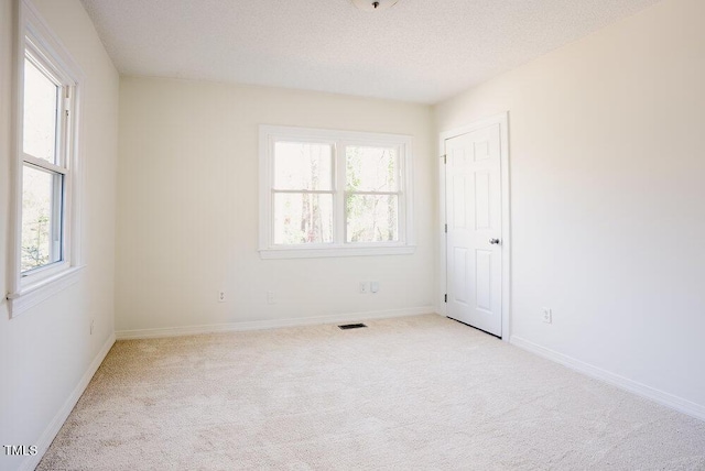 carpeted spare room featuring a textured ceiling, visible vents, and baseboards