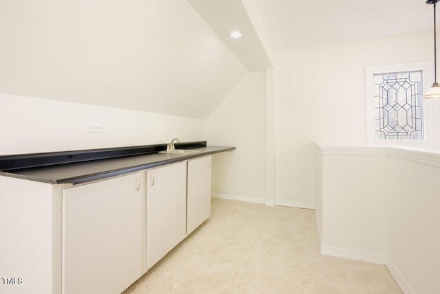 interior space featuring light carpet, baseboards, vaulted ceiling, white cabinetry, and a sink