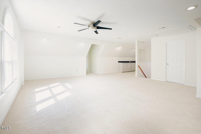 spare room with a textured ceiling, light carpet, a ceiling fan, vaulted ceiling, and attic access