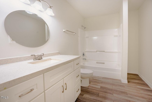 bathroom with toilet, vanity, wood finished floors,  shower combination, and baseboards