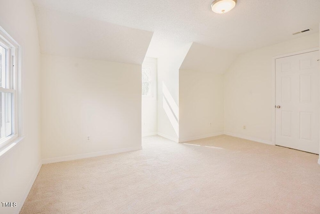 additional living space featuring lofted ceiling, visible vents, a wealth of natural light, and light colored carpet