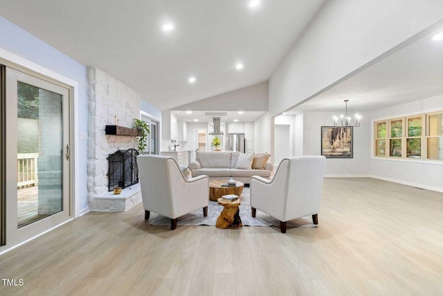 living room featuring light wood-type flooring, a fireplace, a chandelier, and vaulted ceiling