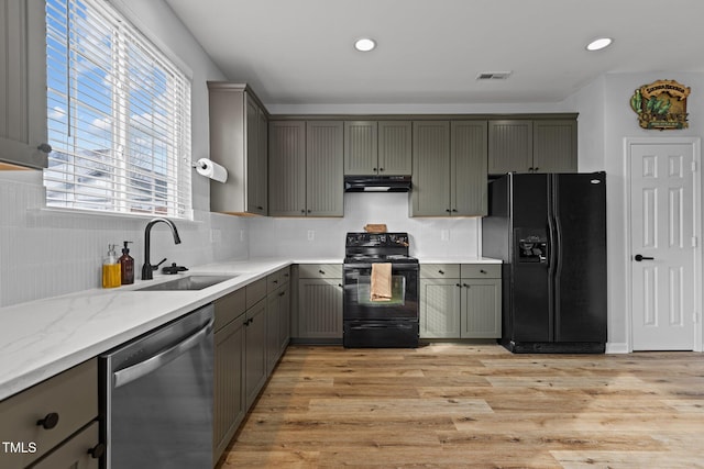 kitchen with light wood-style flooring, under cabinet range hood, a sink, visible vents, and black appliances