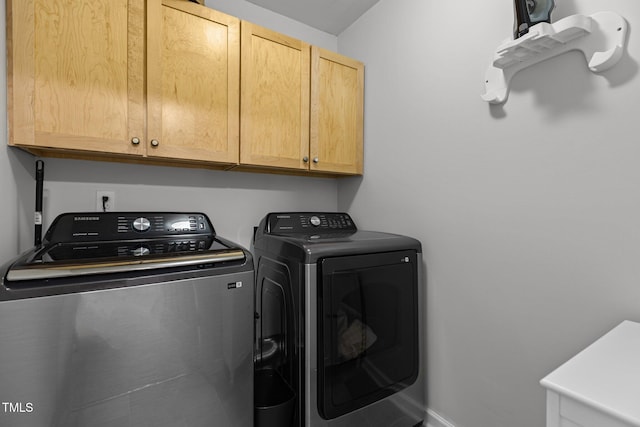 washroom featuring washing machine and dryer, cabinet space, and baseboards