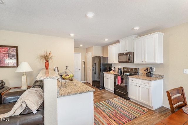 kitchen with open floor plan, black appliances, wood finished floors, and white cabinets