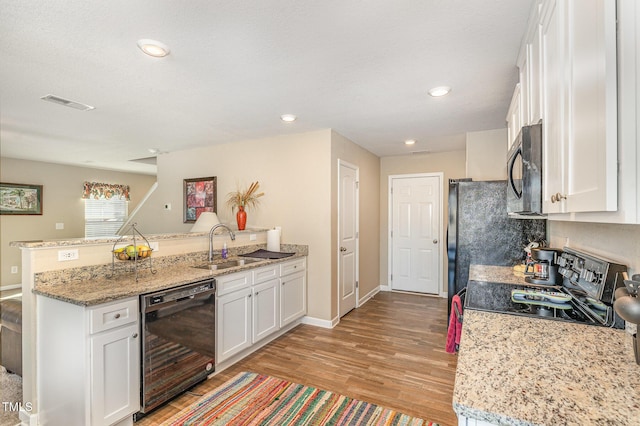 kitchen with a peninsula, black appliances, white cabinetry, and light wood-style floors