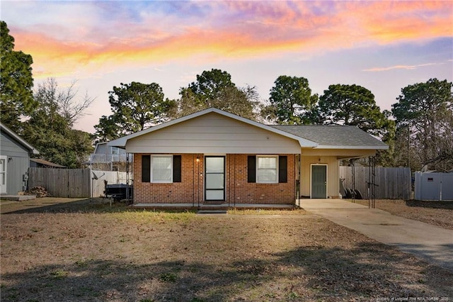 view of front facade with a carport, brick siding, fence, and driveway