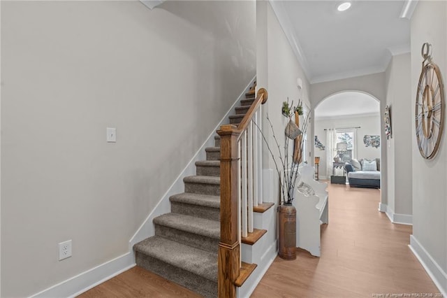 stairs featuring baseboards, crown molding, arched walkways, and wood finished floors