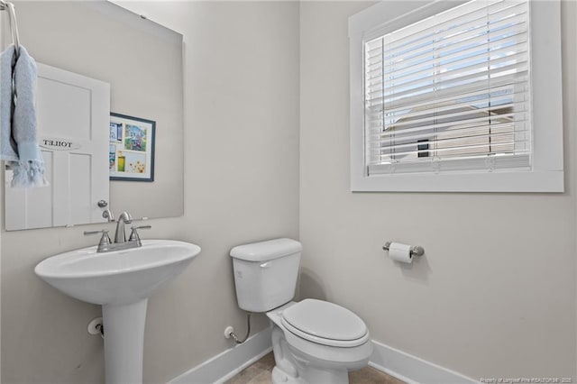 half bathroom with a sink, toilet, and baseboards