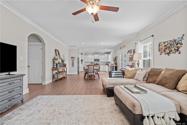 living room featuring arched walkways, light wood-style flooring, and crown molding