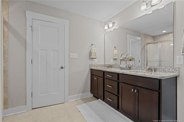 bathroom with double vanity, a stall shower, a sink, and baseboards