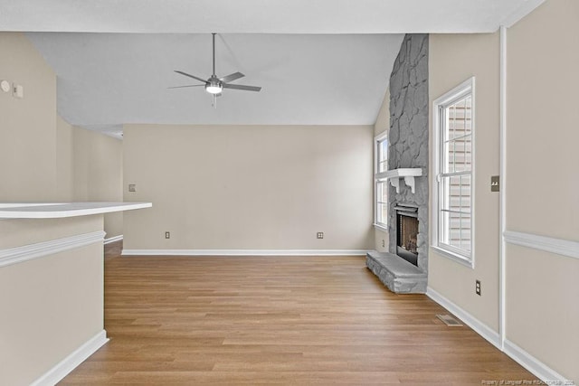 unfurnished living room with visible vents, a ceiling fan, light wood-style flooring, vaulted ceiling, and a stone fireplace