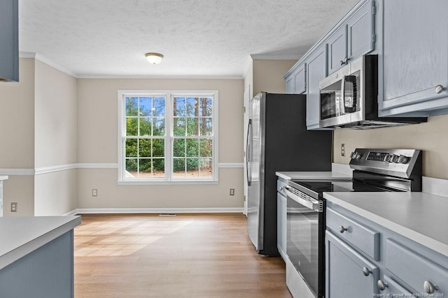 kitchen with appliances with stainless steel finishes, light wood-type flooring, light countertops, and crown molding