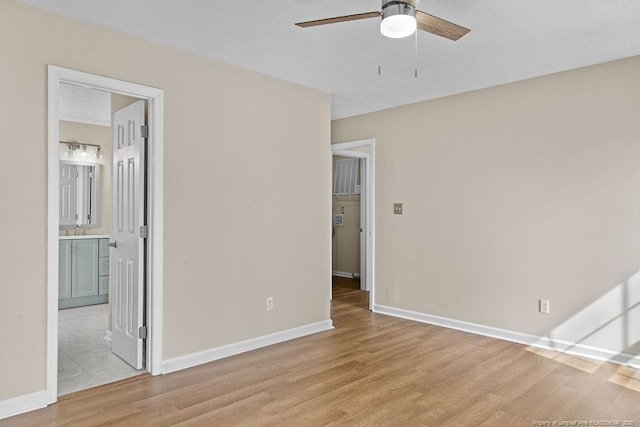 empty room with light wood-style floors, a ceiling fan, baseboards, and a sink